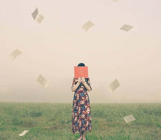 A dream scene shows a woman standing in the middle of a grass field, hiding her face behind a book while the pages fly away.