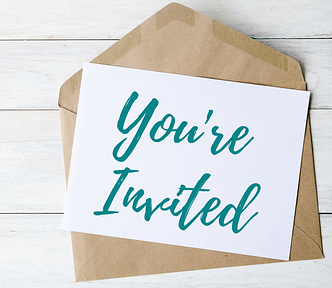 There’s an open brown envelope on a white painted wooden table. A white card placed on it reads “You’re invited” in teal italic handwriting.