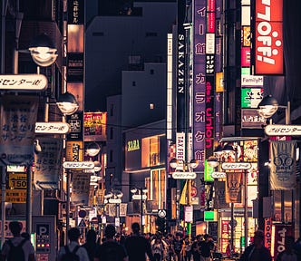 A busy street with neon signs, filled with shops and shoppers.
