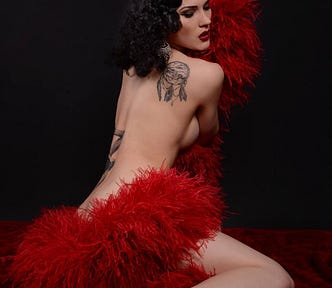 Female body, with tattoos and bold make up, draped with a red feather boa. Burlesque dancer / performer