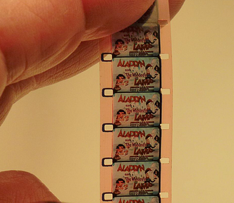 Hand holding up a strip of 16 mm film showing frames from a color cartoon