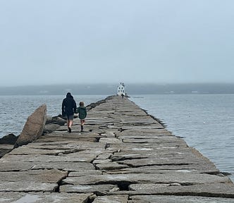 A man and his daughter hold hands and walk along a boardwalk in Maine.