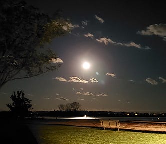 The full moon over Long Island Sound with a bench in the middle ground and grass in the foreground