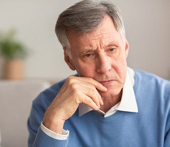 older gentleman looks pensive. Wearing a blue sweater. Gray hair.