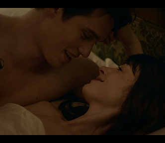 Anne Hathaway and Nicholas Galitzine in ‘The Idea of You’, smiling at each other in bed.