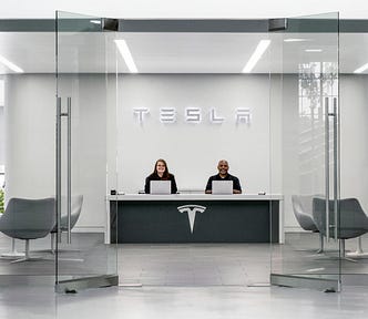 The minimalist front desk at a Tesla office with two people sitting behind laptops at the desk.