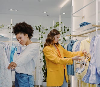 Two young women  look through racks in a clothing store.
