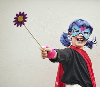 Laughing child with purple hair, red cape, eye mask and wand