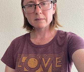 Selfie of author with a little hair on his chest, long hair, and glasses. He’s wearing a “Love Y’all” t-shirt to represent his Southern queer previous life.