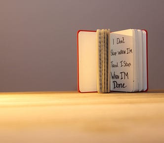 An open book with the words “I don’t stop when I’m tired. I stop when I’m done,” standing upright on a table.