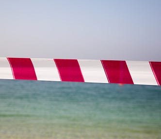 red and white access denied tape blocking off entry to a beautiful seascape