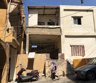 A woman in a headscarf walks past a dilapidated building.