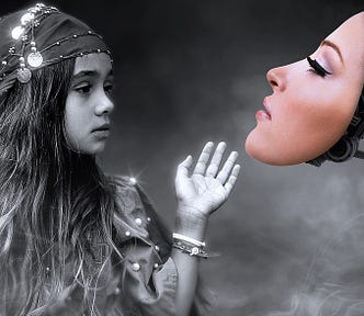 A surreal black and white photo of a young girl with long wavy hair, wearing a bejeweled scarf on her head and a sparkling off-the-shoulder blouse. Her hand adorned with two bangle bracelets and she’s reaching toward a white woman’s face in color, attached to a mechanical arm with multiple gears.