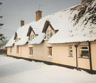 Thatched cottage with gable windows, traditional pink exterior, light covering of snow