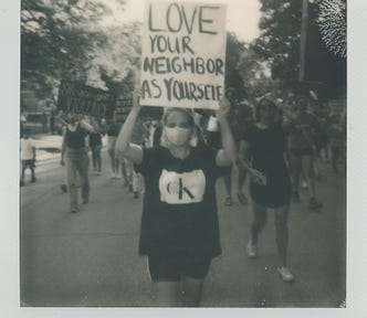 Blurred photo of woman holding up a sign that says love your neighbor as yourself