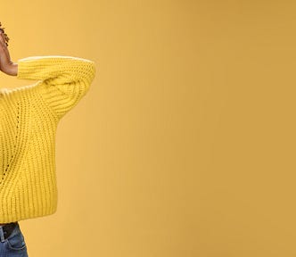 Carefree, happy, attractive girl in a yellow sweater and headband, touching head and smiling broadly. Yellow background.