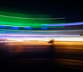 Dynamic time-lapse picture of a motorcycle driving across a backdrop lit with multi-color lights.