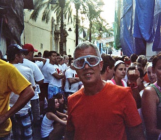 man stands in the middle of a crowded street wearing an orange t-shirt and water goggles.