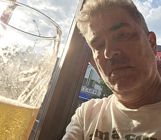 Man sitting by window with half empty glass of beer in front of him.