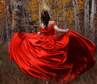 A woman in a red ball gown and gold crown, dancing in front of birch trees in the fall.