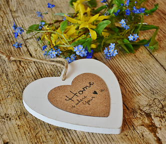 heart decor and flowers placed on a wooden table, written on the heart are the words, “home is where the heart is”