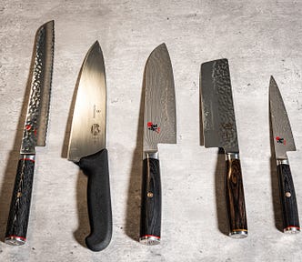 An image of five high quality knives including a bread knife, Chef’s knife, Santoku, Nakiri and Shoto knives.