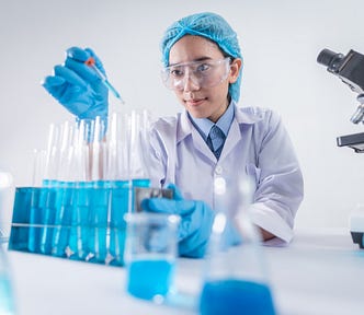 a woman in a lab and full lab kit is pipetting liquid from one test tube of blue liquid to another. She gives off the vibe I wanted to with this article: a focused spirit of scientific inquiry.