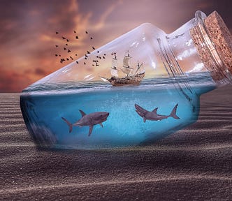 A ship in a bottle, with two sharks beneath in the water. The bottle is corked and rests at an angle in a landscape of rippled sand, and red tinged sky