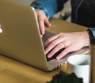 A pair of hands typing on an Apple laptop that is on a desk