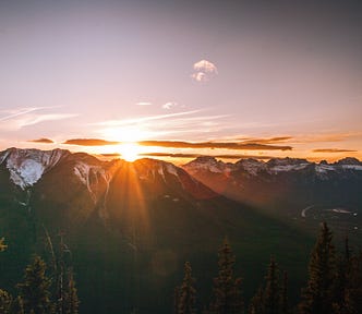 The sun setting behind a mountain range with snowy peaks