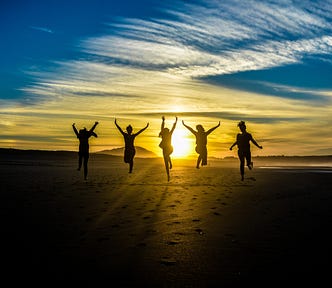 Five silhoutted people raising arms in power against a sunset sky