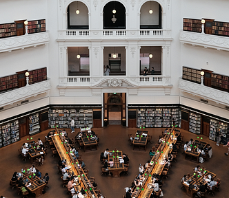 A photo of a grand library reading room with people working at desks and browsing books on shelves