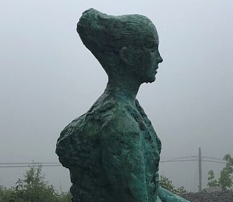 Grey statue of a woman with fog in the background.
