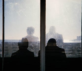 Silhouettes and shadows of two people seen through the dirty glass of a shelter.