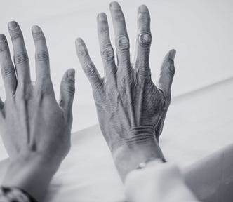 Black and white photograph of a young woman’s hand next to an old woman’s hand