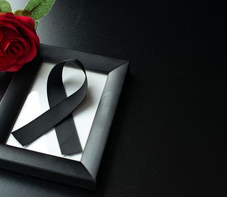 A photo of a picture frame with a black bow on a dark background. There is a red rose to the side.