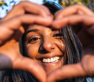 Indian woman making heart sign, and smiling through it.