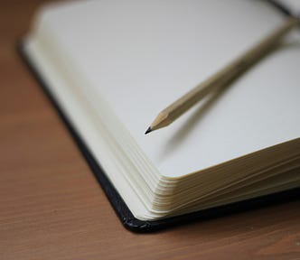 The image is of a pencil lying on the blank page of an open journal. It is a photo by Jan Kahánek on Unsplash.