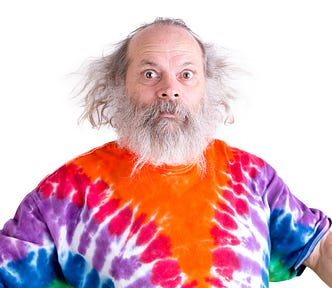 Senior man with grey hair and beard so surprised he’s wide-eyed, he is wearing a tie dye colorful t-shirt