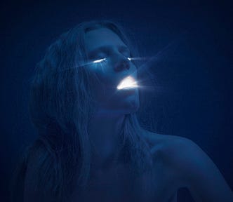 A photo of a woman with light shining from her eyes and mouth. The image is a dark blue/black shade.