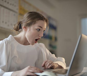 A woman with a surprised face staring at an laptop screen.