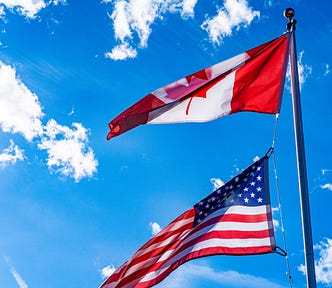 Photo of the Canadian and U.S. flags blowing in the wind against a blue sky