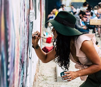 Woman in a green hat, holding a paint can and painting a mural.