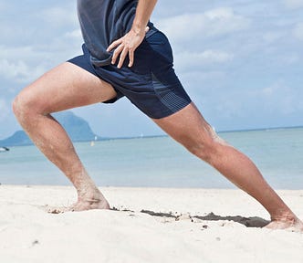 A man stretching his left calf on the beach.