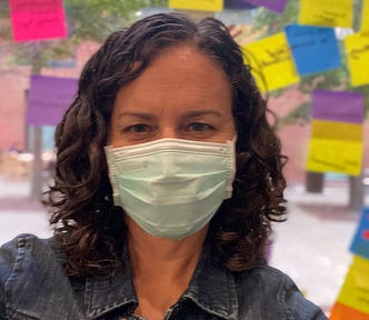 Me wearing a mask and standing in front of colorful post-its after running a design thinking workshop at Wesleyan University, where I currently teach.