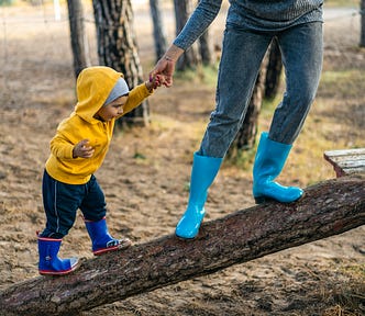 Parent holding hand of small child pulling her up a log.