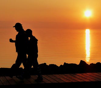 Two people walking beside a lake with their morning coffee at sunrise.