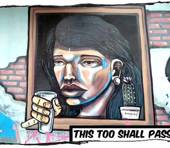 Street painting of a woman looking out a window in a brick wall. She’s holding a glass. The caption reads, “This too shall pass.”