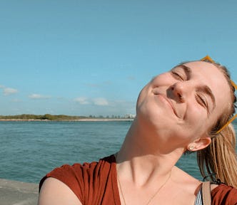 Blonde girl smiling in sun with ocean behind her