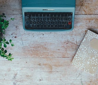 Plant, typewriter, and journal on wooden table.